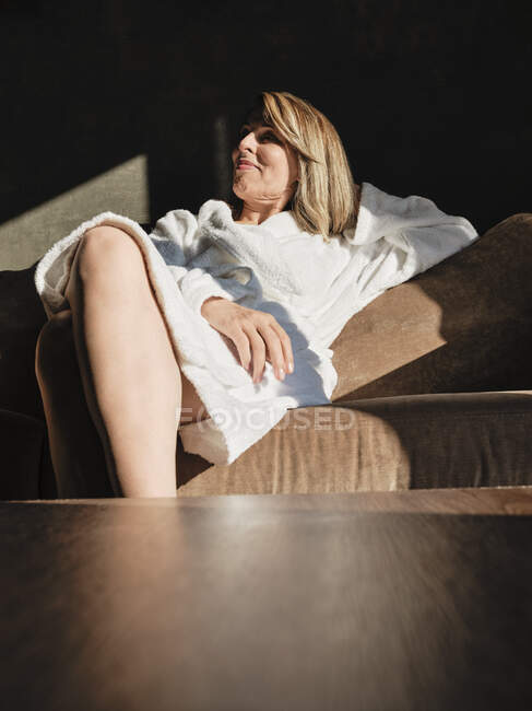 Sorrindo mulher sênior olhando para longe enquanto relaxa no sofá no hotel — Fotografia de Stock