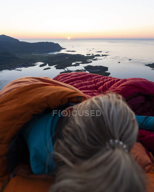 Жінка лежить у спальному мішку проти моря у Воландстіндені (Лофотен, Норвегія). — стокове фото