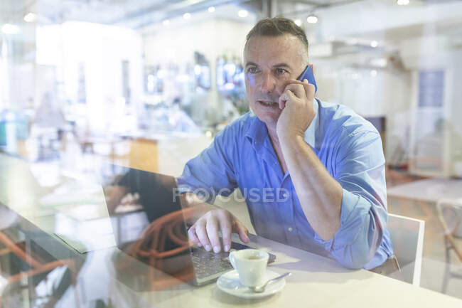 Male professional talking on mobile phone while sitting with laptop and coffee in cafe — Stock Photo