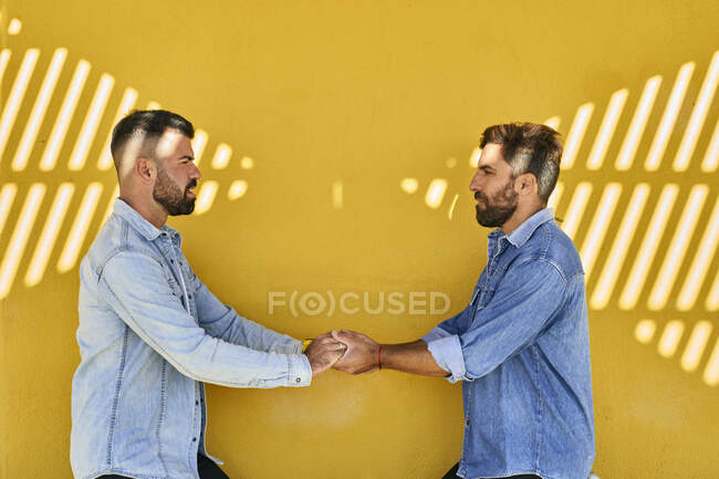 Gay couple holding hands while standing against yellow wall — Stock Photo