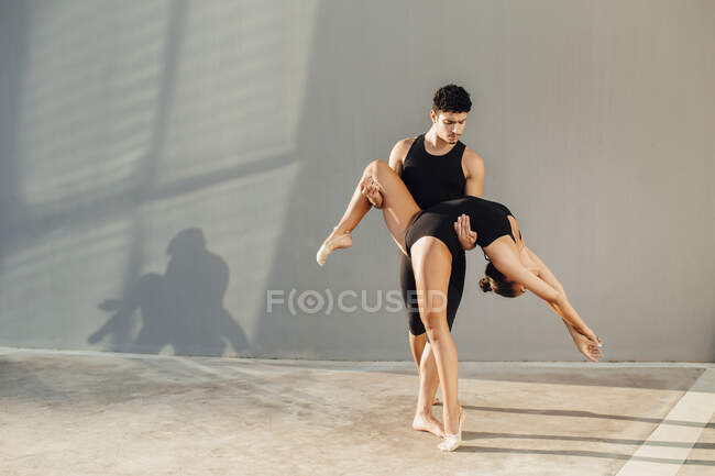 Professional male dancer helping female gymnast in dance pose against wall — Stock Photo