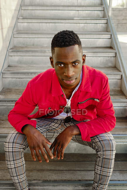 Retrato de jovem de casaco vermelho e calças verificadas sentado em degraus ao ar livre — Fotografia de Stock