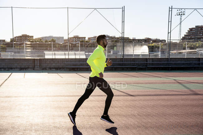 Sportler joggt bei sonnigem Wetter auf Laufstrecke am Sportplatz — Stockfoto