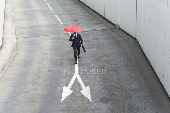 Businessman with red umbrella walking on road marking — Stock Photo