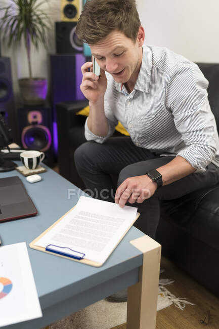 Бизнес-документ проверки во время разговора по мобильному телефону сидя дома — стоковое фото