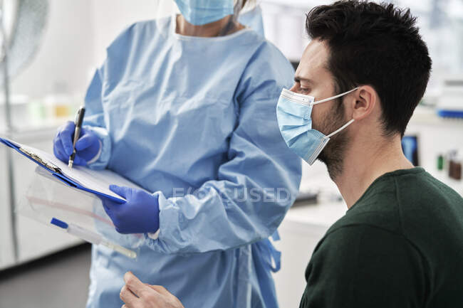 Professionnel médical féminin expliquant les procédures au patient masculin avant de prélever l'échantillon à la clinique — Photo de stock