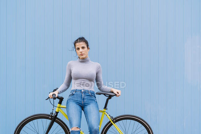 Confident mid adult woman sitting on fixie bike against blue wall —  individuality, portrait - Stock Photo | #481846368