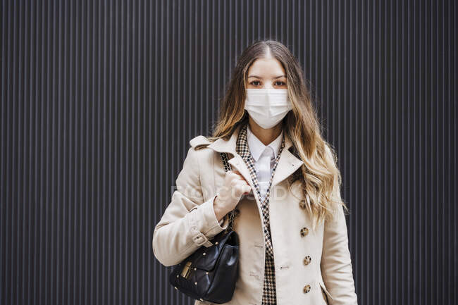 Mid adult woman with purse wearing protective face mask against black wall — Stock Photo