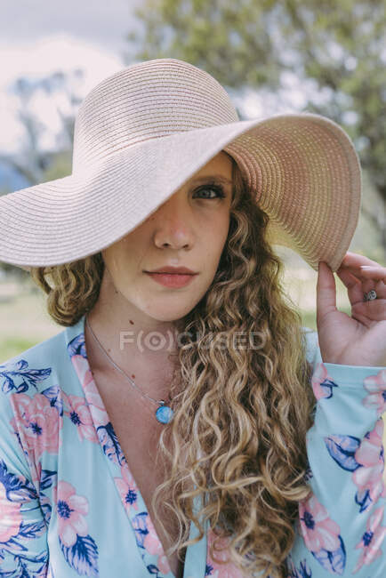 Mujer joven cubriendo ojo con sombrero de sol en el parque - foto de stock