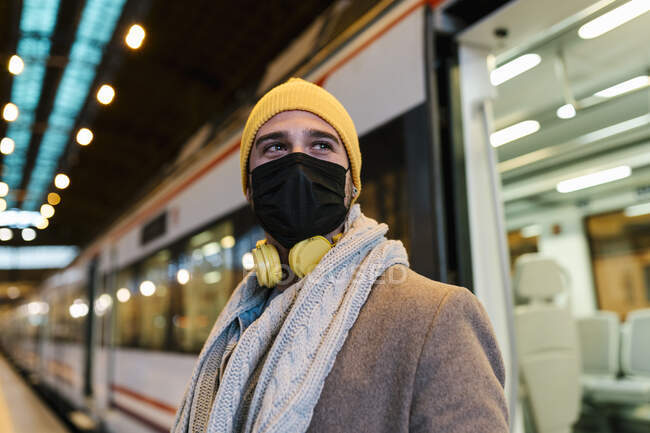 Homem usando máscara facial olhando para longe enquanto estava de pé contra o trem na estação — Fotografia de Stock