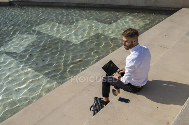 Businessman looking away while sitting with digital tablet on promenade - foto de stock