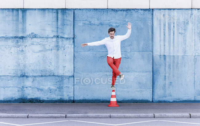 El hombre balanceándose mientras está parado en el cono de tráfico contra la pared azul - foto de stock