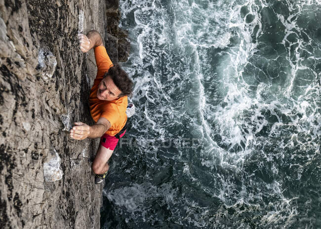 Appassionato scalatore di roccia maschile arrampicata rocciosa scogliera dal mare — Foto stock