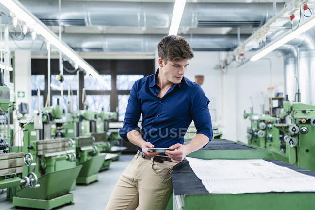 Young businessman looking at floor plan while holding machine part in industry — Stock Photo