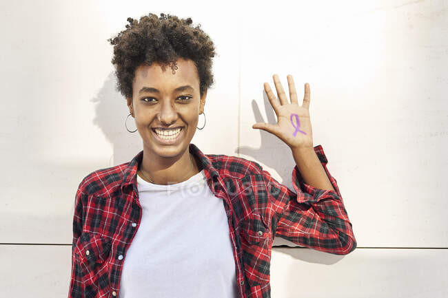 Giovane donna allegra con simbolo di consapevolezza viola sul palmo della mano contro il muro bianco durante la giornata della donna — Foto stock