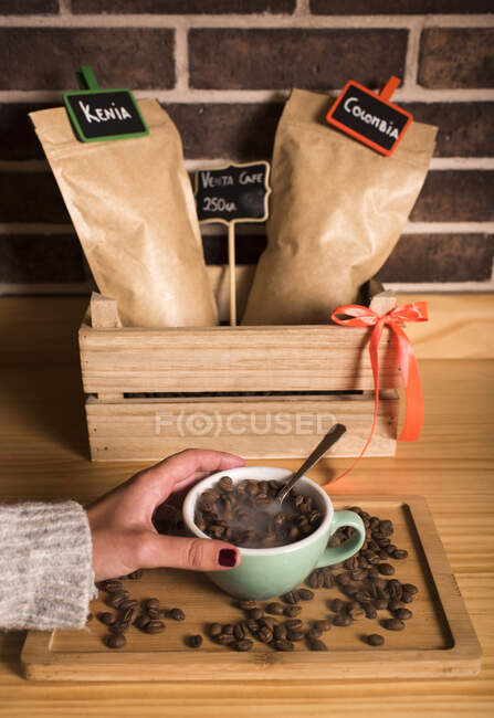 Woman holding coffee cup with beans inside at cafe — Stock Photo