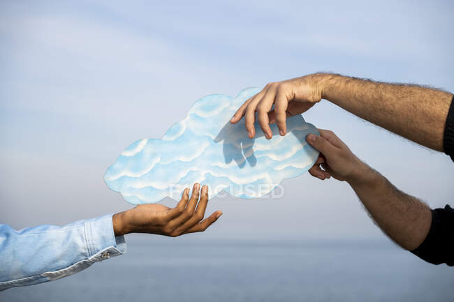 Gente sosteniendo nubes cortadas contra el cielo - foto de stock