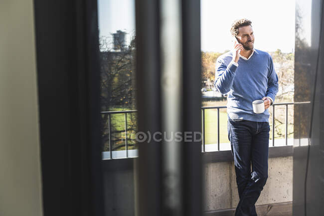 Бізнесмен з чашкою кави розмовляє по мобільному телефону, стоячи біля офісного балкона. — стокове фото