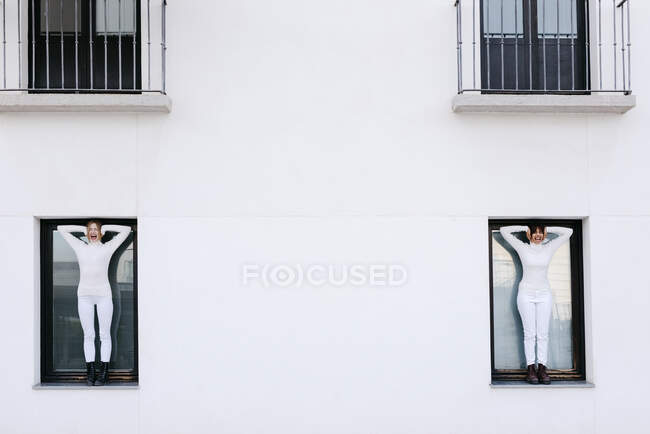 Giovani donne in piedi su finestre di edificio bianco urlando mentre coprono le orecchie durante COVID-19 — Foto stock
