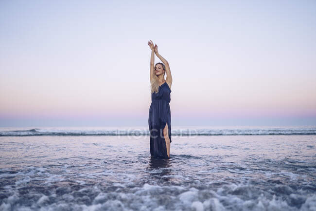 Fashionable woman standing with hand raised at Platja de Llevant beach during sunset — Stock Photo