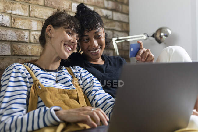 Lesbian couple looking at credit card while doing online shopping on laptop at home — Stock Photo