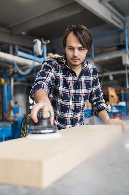 Manual worker sanding wood with sander while standing at industry — Stock Photo