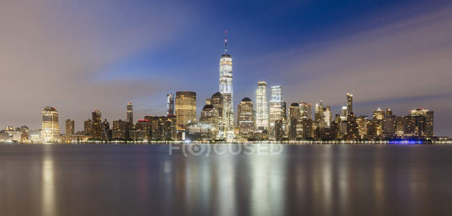USA, New York, New York City, Lower Manhattan with One World Trade Center illuminated at dawn seen across river - foto de stock