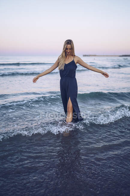 Mujer joven de pie con los brazos extendidos mientras juega en la playa Platja de Llevant - foto de stock