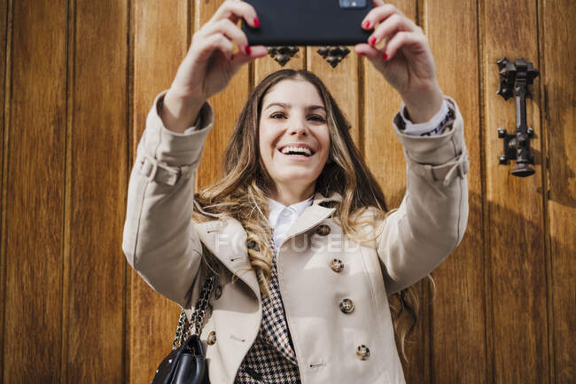 Allegro donna prendendo selfie mentre in piedi contro porta di legno — Foto stock