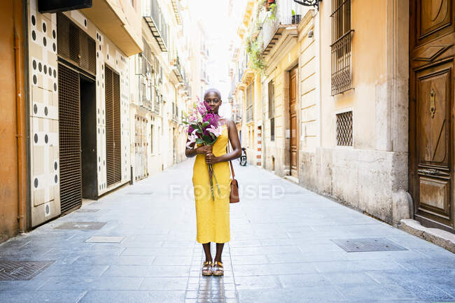 Mujer con expresión en blanco sosteniendo flores mientras está de pie en la calle de la ciudad - foto de stock