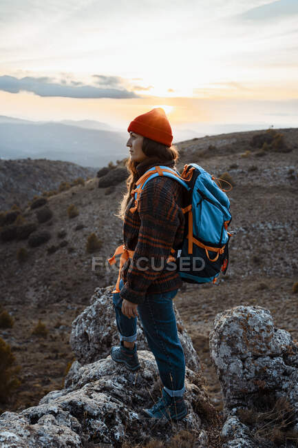 Ragionevole escursionista donna distogliendo lo sguardo mentre in piedi sulla montagna rocciosa durante il tramonto — Foto stock