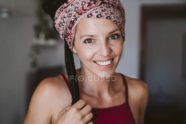 Mujer adulta mediana con pañuelo en la cabeza sonriendo mientras está de pie en casa - foto de stock