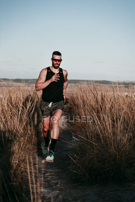 Confident male athlete running in dried grass field against sky — Stock Photo