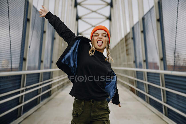 Joyeux jeune femme avec les yeux fermés collant la langue tout en dansant sur la passerelle — Photo de stock