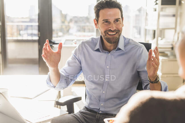 Uomo d'affari sorridente che discute con un collega mentre siede in ufficio — Foto stock