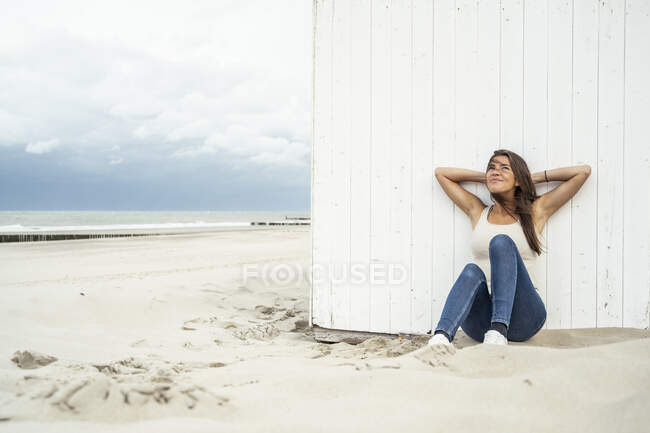 Smiling woman with hands behind head leaning on wall at beach — Stock Photo