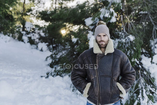 Junger Mann mit Händen in Hosentaschen gegen Bäume im Schnee — Stockfoto