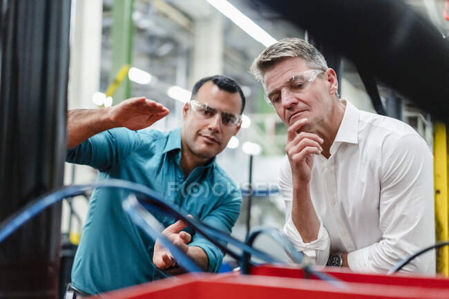 Коллеги-мужчины в очках, осматривающие производственное оборудование в промышленности — стоковое фото