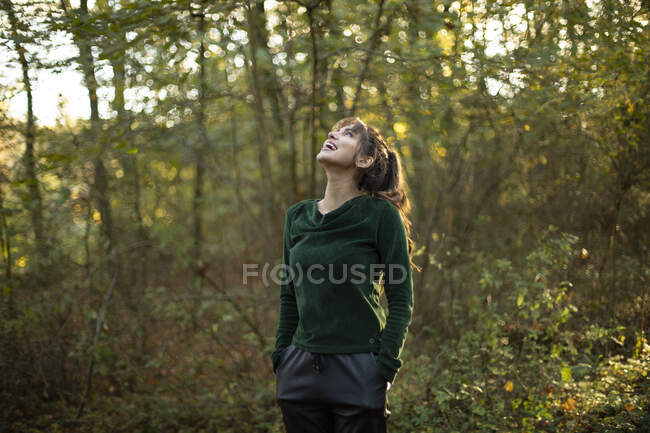Femme heureuse avec les mains dans les poches levant les yeux tout en se tenant dans le parc public — Photo de stock