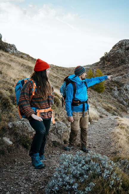 Взрослый мужчина указывает во время похода с подругой на скалистую гору во время отпуска — стоковое фото
