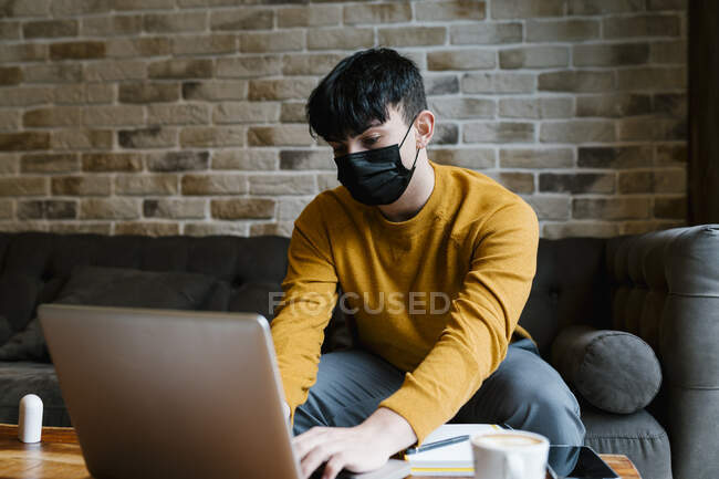 Mann trägt Mundschutz mit Laptop, während er während der COVID-19 im Café sitzt — Stockfoto