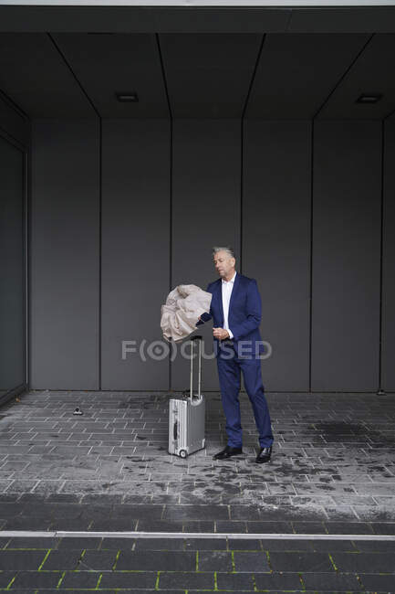 Businessman with luggage opening umbrella while standing at footpath — Stock Photo