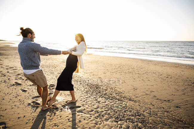 Couple joyeux tenant la main tout en dansant sur la plage contre le ciel clair pendant la journée ensoleillée — Photo de stock