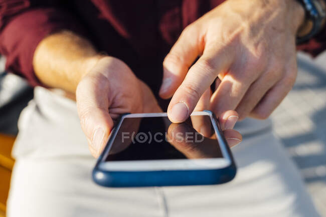 Businessman pointing at smart phone screen while sitting outdoors - foto de stock
