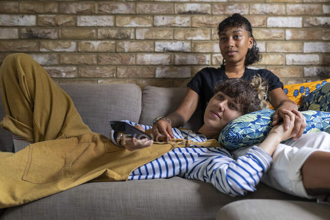 Girlfriend resting on woman's lap while watching tv at home — Stock Photo