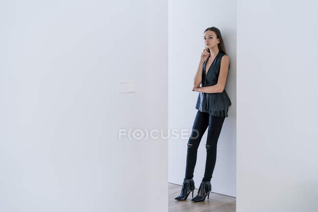 Дівчинка - підліток, одягнена в стильний одяг, спирається на стіну вдома, яку видно через коридор. — стокове фото