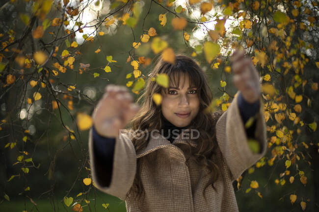 Smiling woman holding branch while standing in park during autumn — Stock Photo