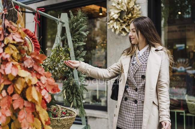 Модна жінка торкається листя, стоячи в квітковому магазині — стокове фото
