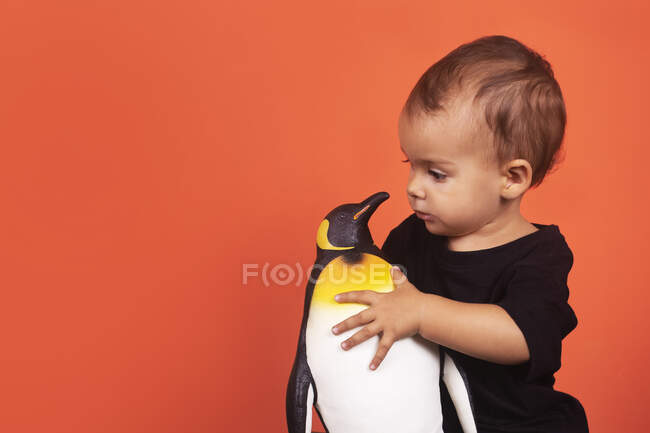 Bambino ragazza giocare con pinguino giocattolo mentre seduto su sfondo arancione — Foto stock