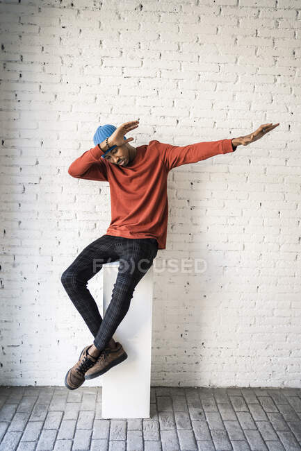 Uomo tamponamento mentre seduto sul piedistallo contro muro di mattoni bianchi — Foto stock